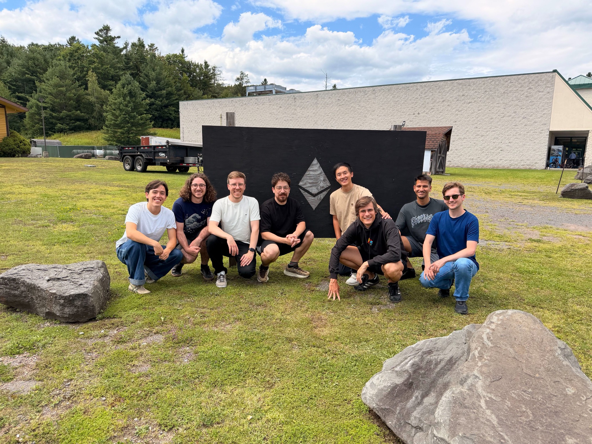 The Ethlabs team crouching in front of a black wooden board with a carved Ethereum logo, in Hunter, NY